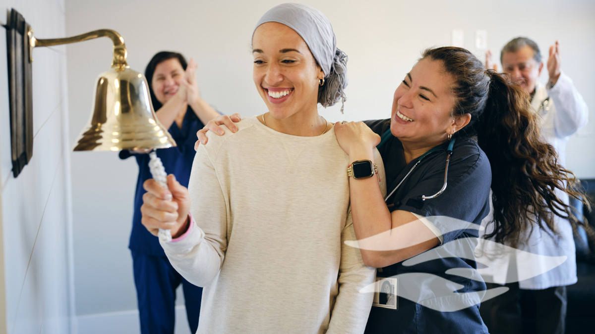 An adult woman chemotherapy patient in a treatment office, celebrating the completion of her treatment with a ceremonial bell ring.