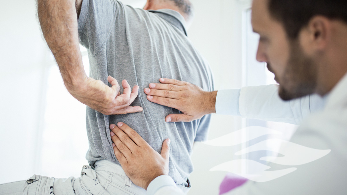 Closeup rear low angle view of an early 60's senior gentleman having some back pain. He's at doctor's office having medical examination by a male doctor. The patient is pointing to his lumbar region.