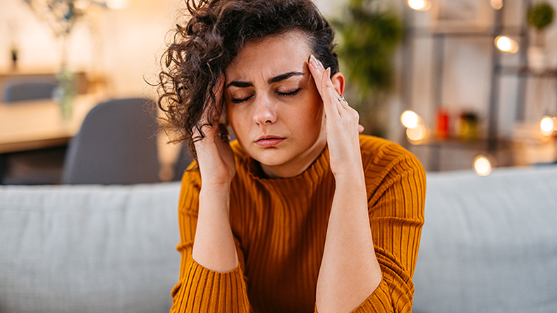 Young woman sitting on the sofa holding her head