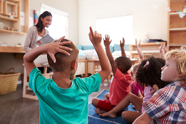 Young children raising hands during story time in a classroom