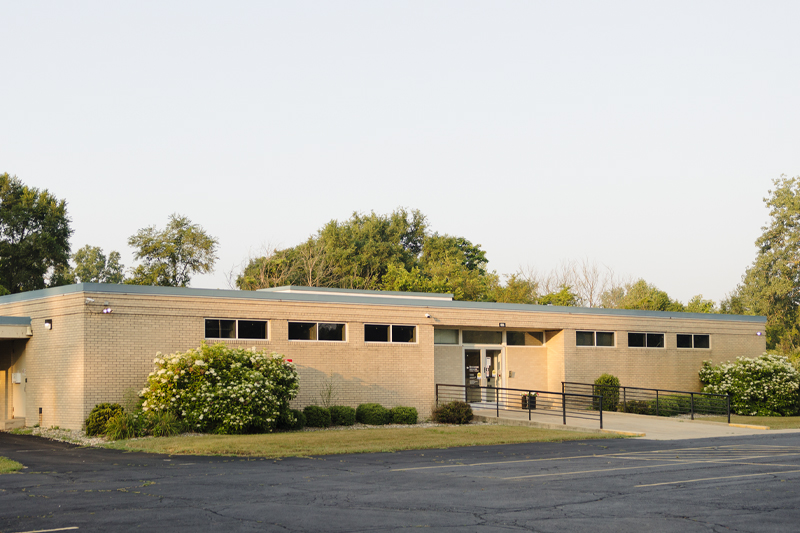Front view of Riverside Medical Group Primary Care – Pembroke brick clinic, showing main entrance with an accessible ramp and flowering shrubs.