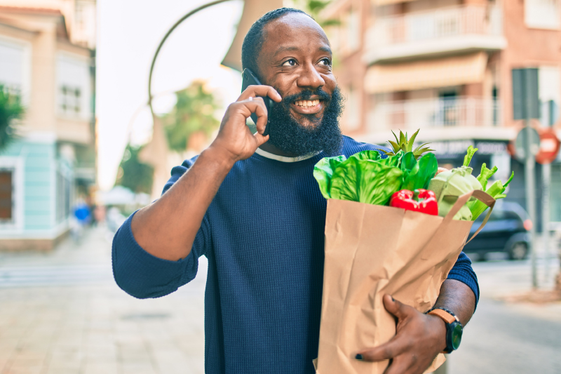 Man scheduling his annual primary care checkup on the phone while carrying groceries.