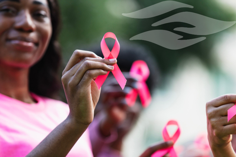 Smiling woman in a pink shirt holding up a pink breast cancer awareness ribbon.