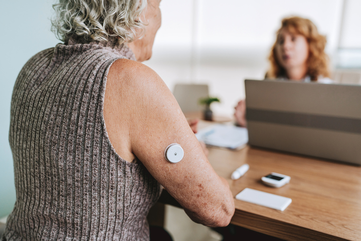 Senior woman with glucose meter on her arm speaking to a doctor