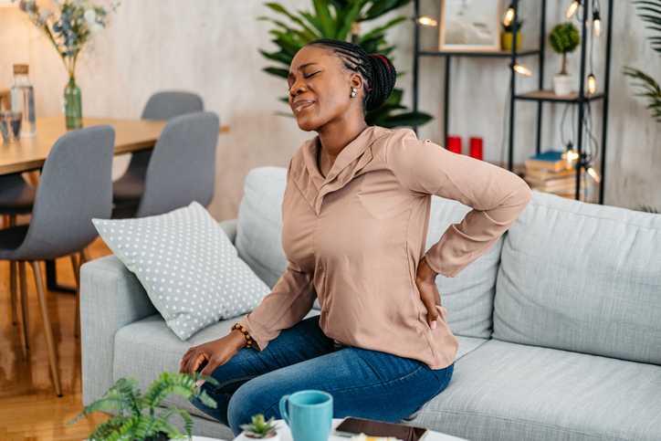 Young Woman Having Back Pain While Sitting On The Sofa At Home