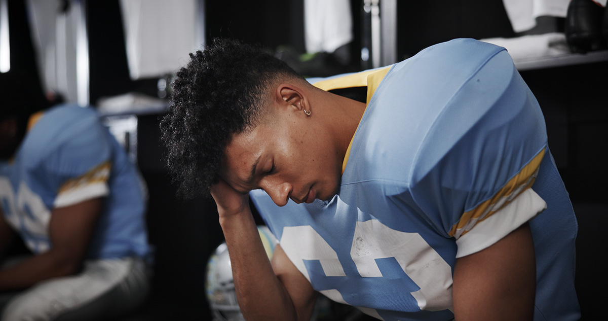 Football player in a locker room holding his head as if injured