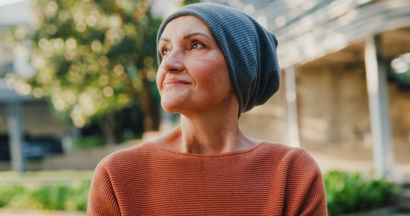 A woman, bald from cancer treatment, wearing a beanie and looking off into the distance