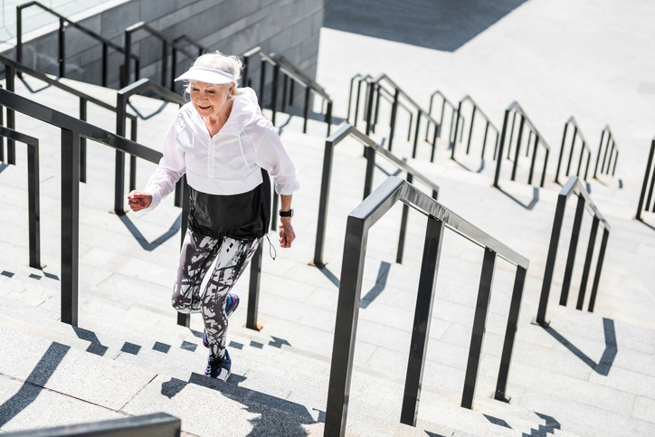 Smiling senior woman walking up a set of stairs outdoor, smiling and pain-free