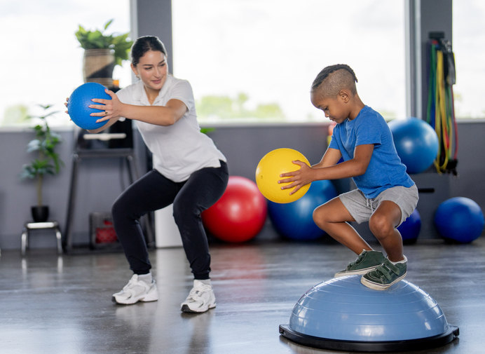 Pediatric physical therapist helping a young child practice balance and walking during a therapy session.