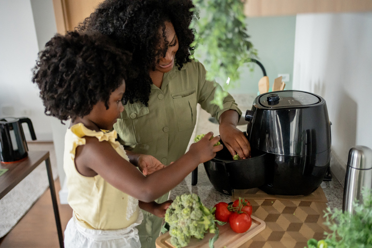 A mother and daughter preparing vegetables in an air fryer for a healthy meal.