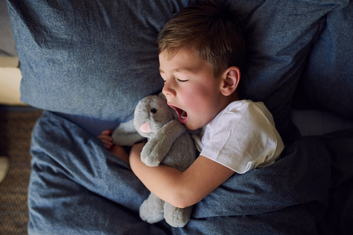 Young boy yawns while laying in bed