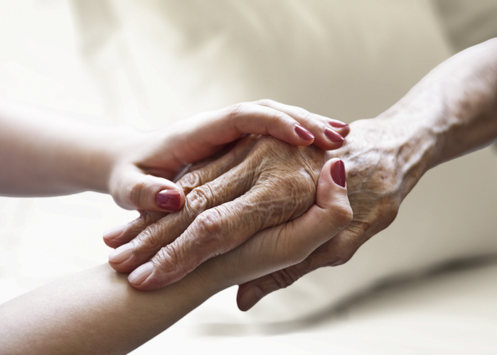 Woman holding senior woman's hand on bed