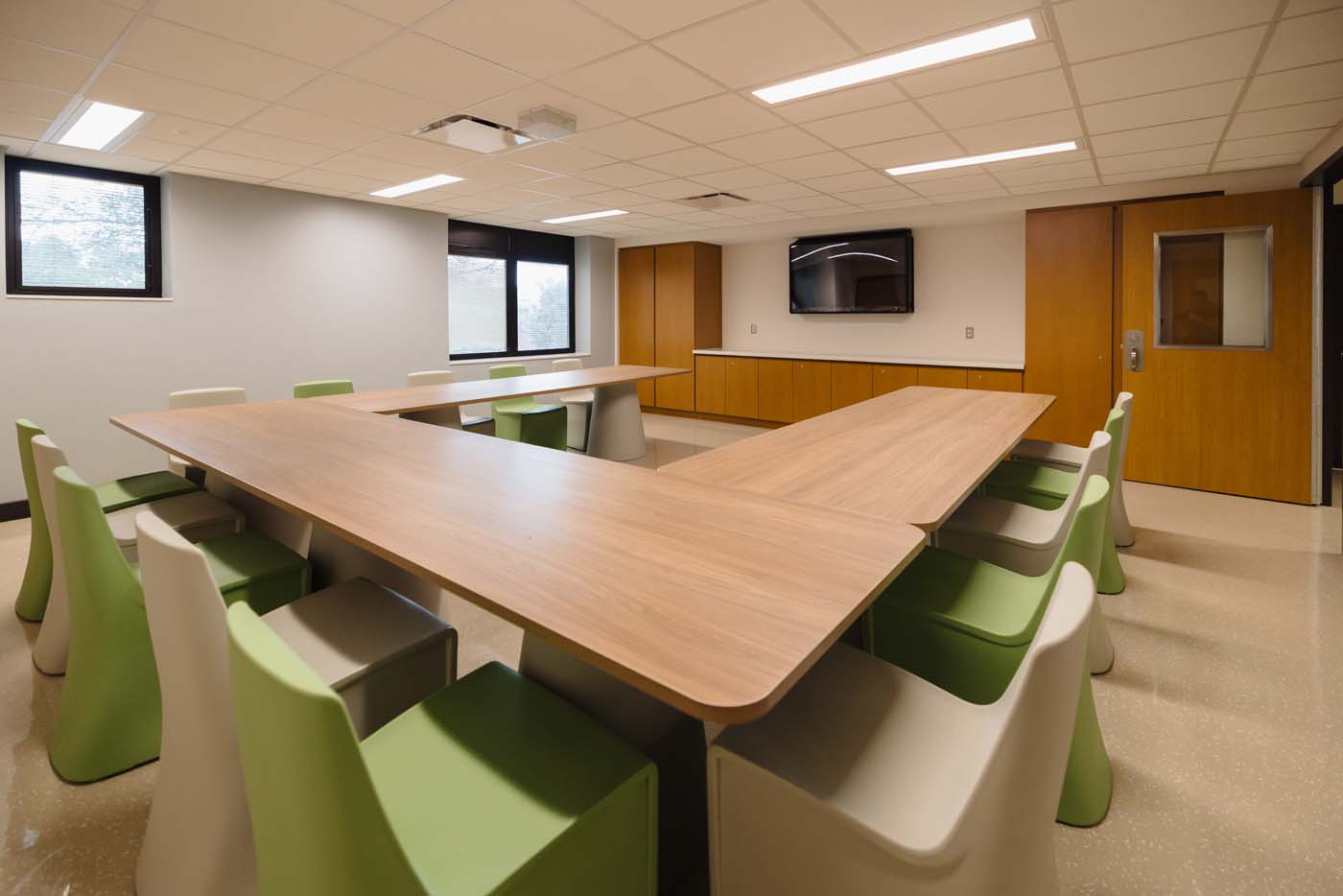 Group room with a long wood table and green chairs for patient programming.