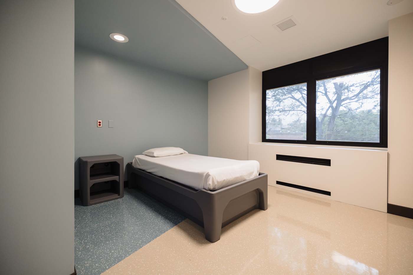 Patient room with a built-in nook, bed and window in calming colors.